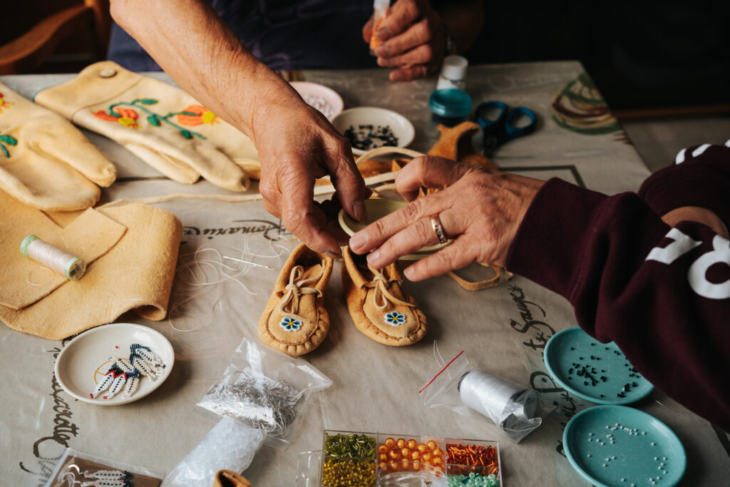 Image showing the hands of a B.C. First Nations woman working on beading on a pair of baby moccasins. Image is part of a story about Indigenous arts funding. Image by Julie Elizabeth Photography. opportunities in B.C.