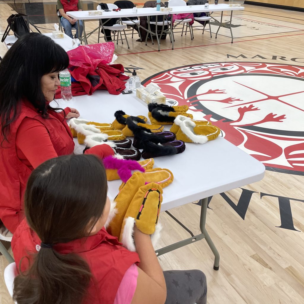 A woman and girls at a table full of hand-made moccasins as part of a cultural documentary project.