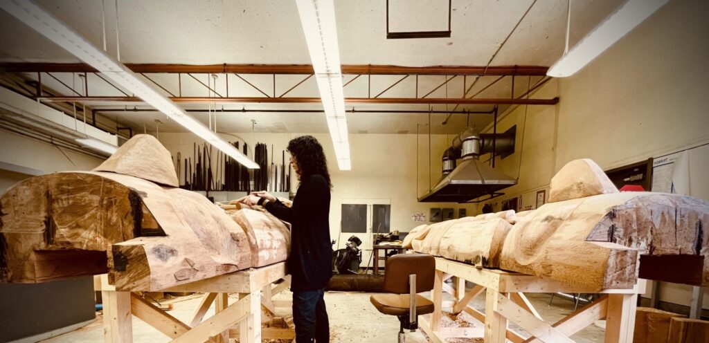 Image of a woman standing at carving pole with another behind her in a B.C. First Nations carving space supported by First Nations Arts infrastructure Program funding in B.C.