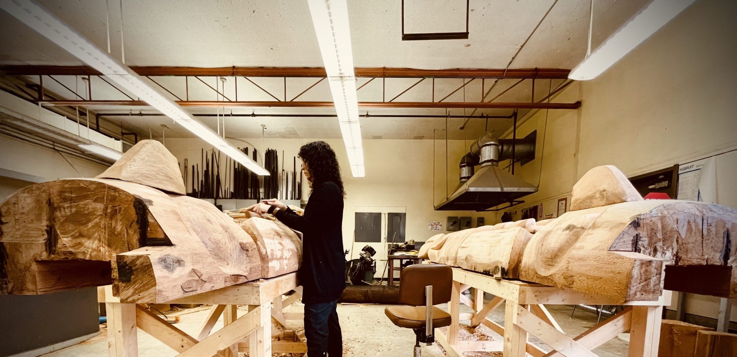 Image of a woman standing at carving pole with another behind her in a B.C. First Nations carving space supported by First Nations Arts infrastructure Program funding in B.C.