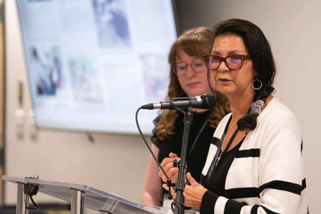 Diane Dejarlais, West Moberly First Nations at a microphone speaking at the 202024 FPCC Heritage Forum. She shared about the economic